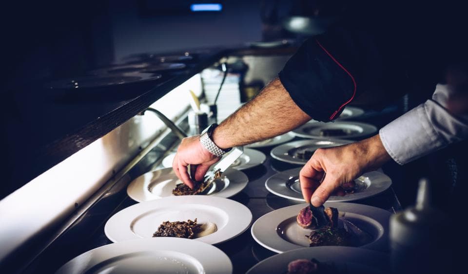 A chef plating dishes along a restaurant pass